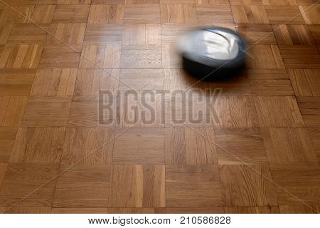 Modern robotic vacuum cleaner on laminate wooden floor, natural movement, natural motion blur