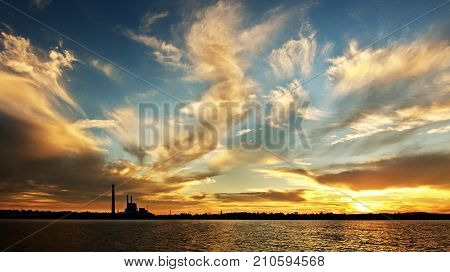 A striking inspirational gold coloured cloudy salt water lake sunset over a power station with water reflections. Captured on Lake Macquarie Australia.
