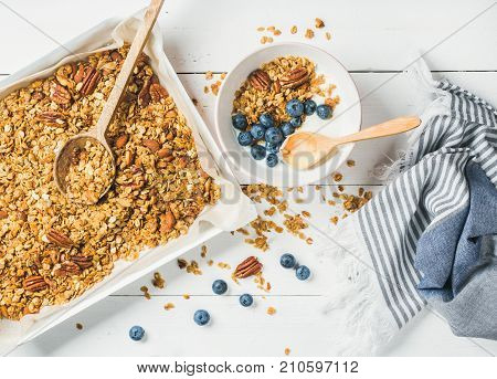 Healthy breakfast. Oat granola with pecan nuts, yogurt and blueberry in bowl on white wooden background, top view