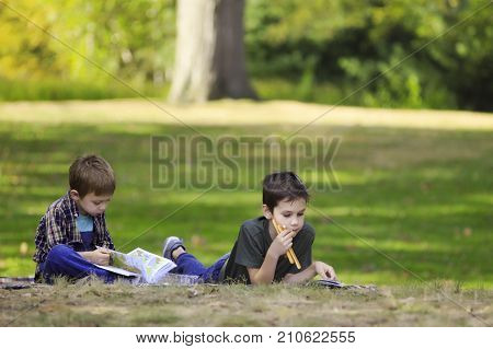 children lie on the grass and read books. boys eating breadsticks and reading outdoors. The concept of the home schooling