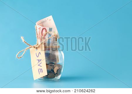saving money in jar on plain blue background