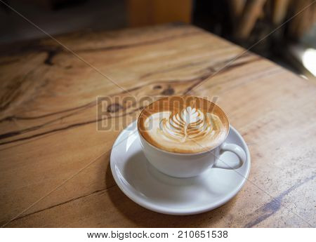 Cup of tasty cappuccino is standing on the wooden textured table. Cappuccino is in the white big cup.