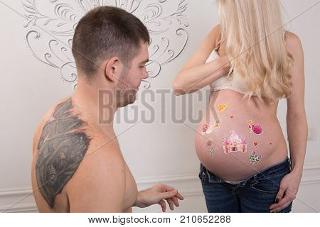 Beautiful pregnant couple in love on the background. Hands of husband on the tummy of his pregnant wife. Young man tenderly stroked pregnant belly of his wife. Husband kissing pregnant belly.