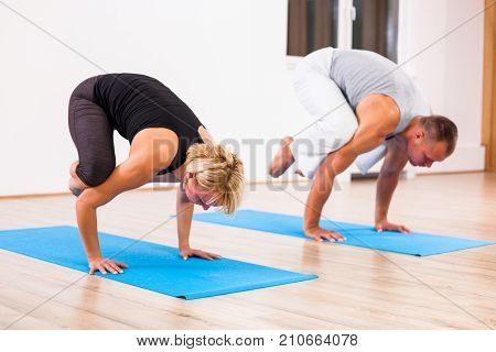 Adult man and woman practicing yoga, Bakasana / Crane pose