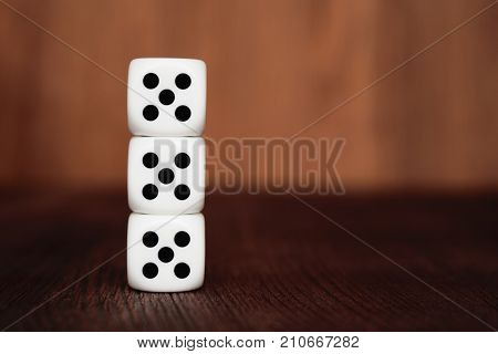 Three white plastic dices on each other on brown wooden board background. Six sides cube with black dots. Number 555.