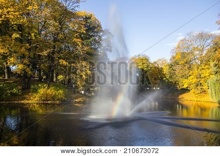 Fountain and rainbow in Riga Canal that flows through Bastion park autumn background with colored leaves (Bastejkalns). Latvia autumn