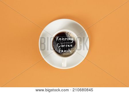Top view of cup of black coffee and Keeping coffee fresh lettering isolated on orange background. Still life. Mock up. Flat lay