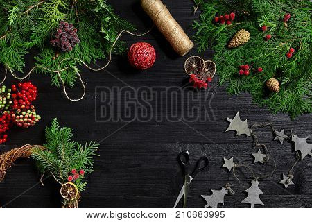 Make a Christmas wreath with your own hands. Spruce branch, Christmas wreath and gifts on a black wooden background. Workplace for preparing handmade decorations.