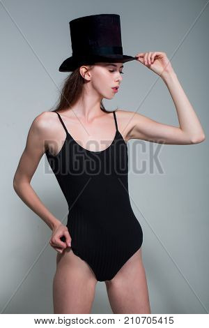 Fashion model pose in studio on grey background. Beauty and fashion. Look and fashion style.. Woman with long brunette hair and no makeup. Girl in black fashionable swimsuit and hat.