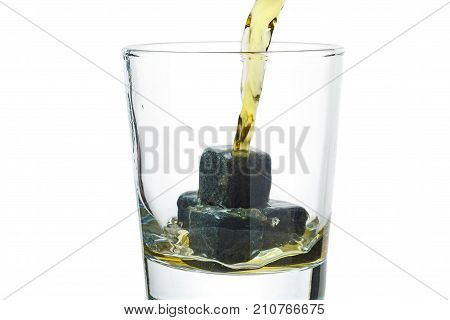 Whiskey pours into a glass with stones.