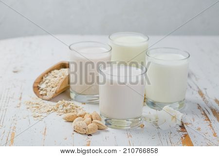 Non-dairy milk alternatives in glasses on white wood background