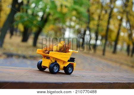 A Small Toy Yellow Truck Is Loaded With Yellow Fallen Leaves. The Car Stands On A Wooden Surface Aga