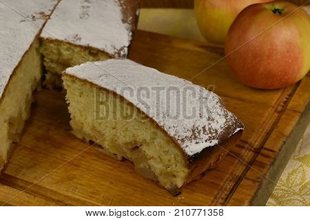 piece of apple pie powdered with sugar powder charlotte on a wooden board with whole apples