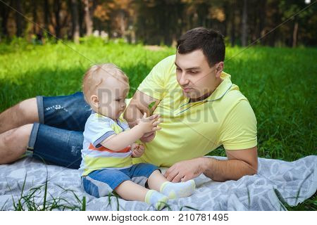 handsome man resting with his son in forest, young guy playing with little son in park