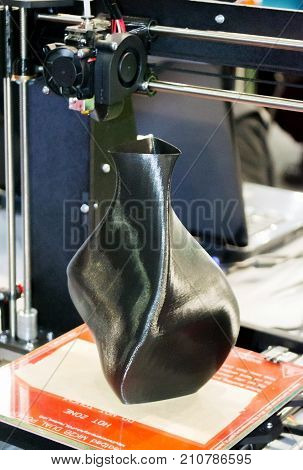 3D printer printing a model in the form of black vase close-up. The concept modern additive technology. The 4ht industrial revolution.