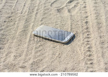 Lost white smartphone with crack on the screen lying in the sand