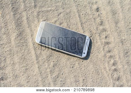 Lost white smartphone with crack on the screen lying in the sand