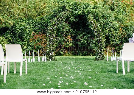 Place for wedding ceremony with white chairs and an arch of living plants