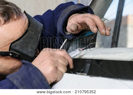 Repair cracked windshield. Fitter uses a syringe for applying the adhesive.