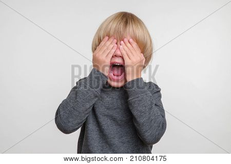 Funny little boy in a gray pullower posing on the camera in studio. Happy smiling child on the gray background. Close-up of little boy.