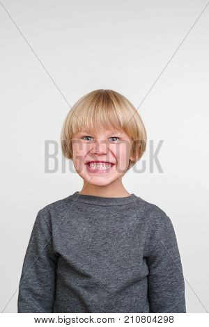 Funny little boy in a gray pullower posing on the camera in studio. Happy smiling child on the gray background. Close-up of little boy.