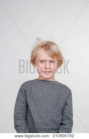 Funny little boy in a gray pullower posing on the camera in studio. Happy smiling child on the gray background. Close-up of little boy.