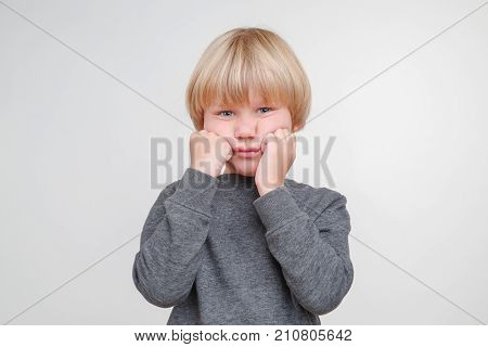 Funny little boy in a gray pullower posing on the camera in studio. Upset child on the gray background. Close-up of little boy.