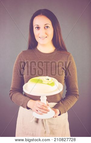 Portrait of young pastre shef with cake on gray background.