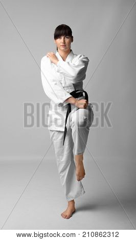 Young woman practicing karate on light background