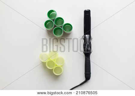 hair tools, beauty and hairdressing concept - curling iron or hot styler and curlers on white background