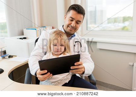 medicine, healthcare, pediatry and people concept - happy doctor or pediatrician holding little girl patient with tablet pc computer in medical office at clinic