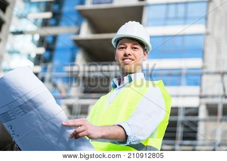 Construction engineer studying floor plan in front of building shell at construction site