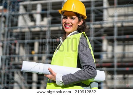 Female civil engineer with construction plans at building site of high-riser