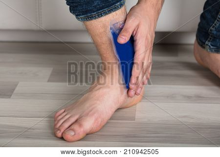 Close-up Of Person's Hand Holding Ice Gel Pack On Ankle At Home