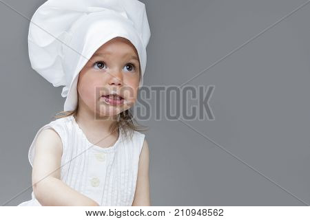 Portrait of Caucasian Little Girl in Cook Uniform Posing with Smudgy Face Against Gray Background. Horizontal Image