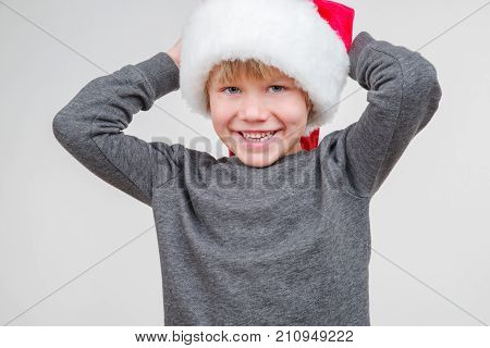 Little blond emotional boy in a festive red hat in a gray jacket