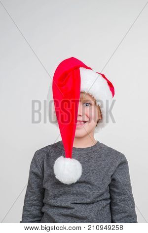 Little blond emotional boy in a festive red hat in a gray jacket. Little Santa Claus