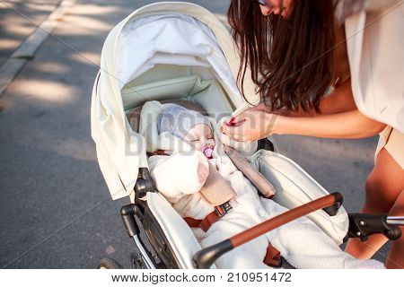 Mom young holds a child's hand in a white stroller in the street