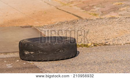 Closeup of old tire without tread and showing sever signs of wear laying on pavement next to concrete walkway