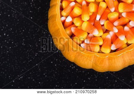 Ceramic pumpkin bowl filled with Halloween candy corn. Top view with dark background.