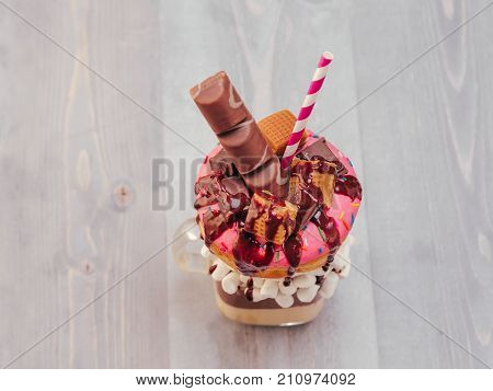 Chocolate and donuts extreme milkshake with marshmallow and other sweets in mason jar on gray wooden background. Crazy freakshake on gray wooden table with copy space