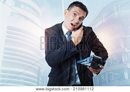 Busy line. Nice cheerless stressed out businessman having a landline phone in his hands and holding a receiver while making a call