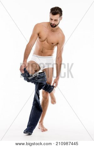 One more move. Full length of handsome shirtless young man taking off his jeans and looking away while standing against white background.