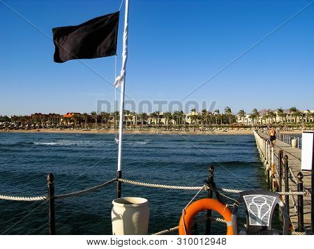The Red Sea Coast In Sharm El-sheikh, Egypt, Sinai, Rough Sea Waves, A Black Flag On The Pier Warns 