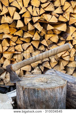 Axe In A Stump Near The Stack Of Chopped Firewood Logs. Wood Splitting. Close-up.