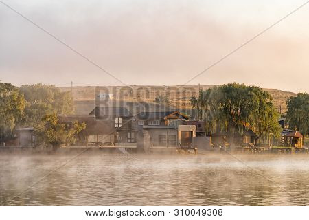 Vrede, South Africa - May 2, 2019: Holiday Homes Are Visible Through The Mist At Sunrise On The Dam 
