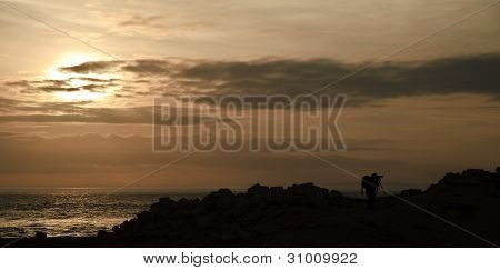 Silhueta de fotógrafo de paisagem contra falésias e o impressionante céu do sol vibrante