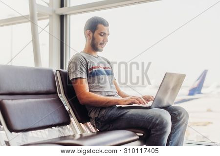 Young Man Using Laptop In Airport Terminal