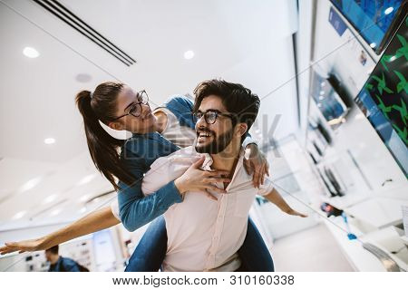 Beautiful Hipster Cheerful Couple Having Fun And Piggyback Ride While Buying In The Electronic Store