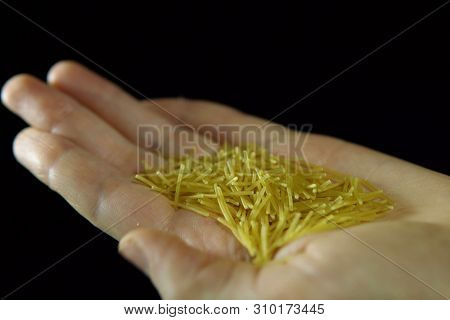 Close-up Of Human Fingers Move A Handful Of Vermicell In Hand On A Black Background, Unrecognizable 